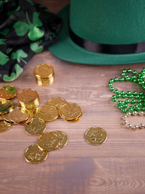 Fotomural Accesorios festivos del Día de San Patricio con monedas de oro y patrones de trébol sobre superficie de madera.