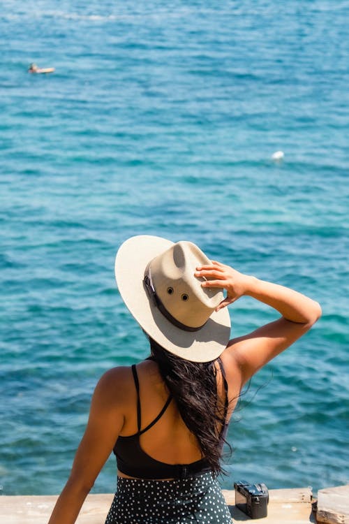 A Woman in Swimwear Wearing a Hat Near Body of Water