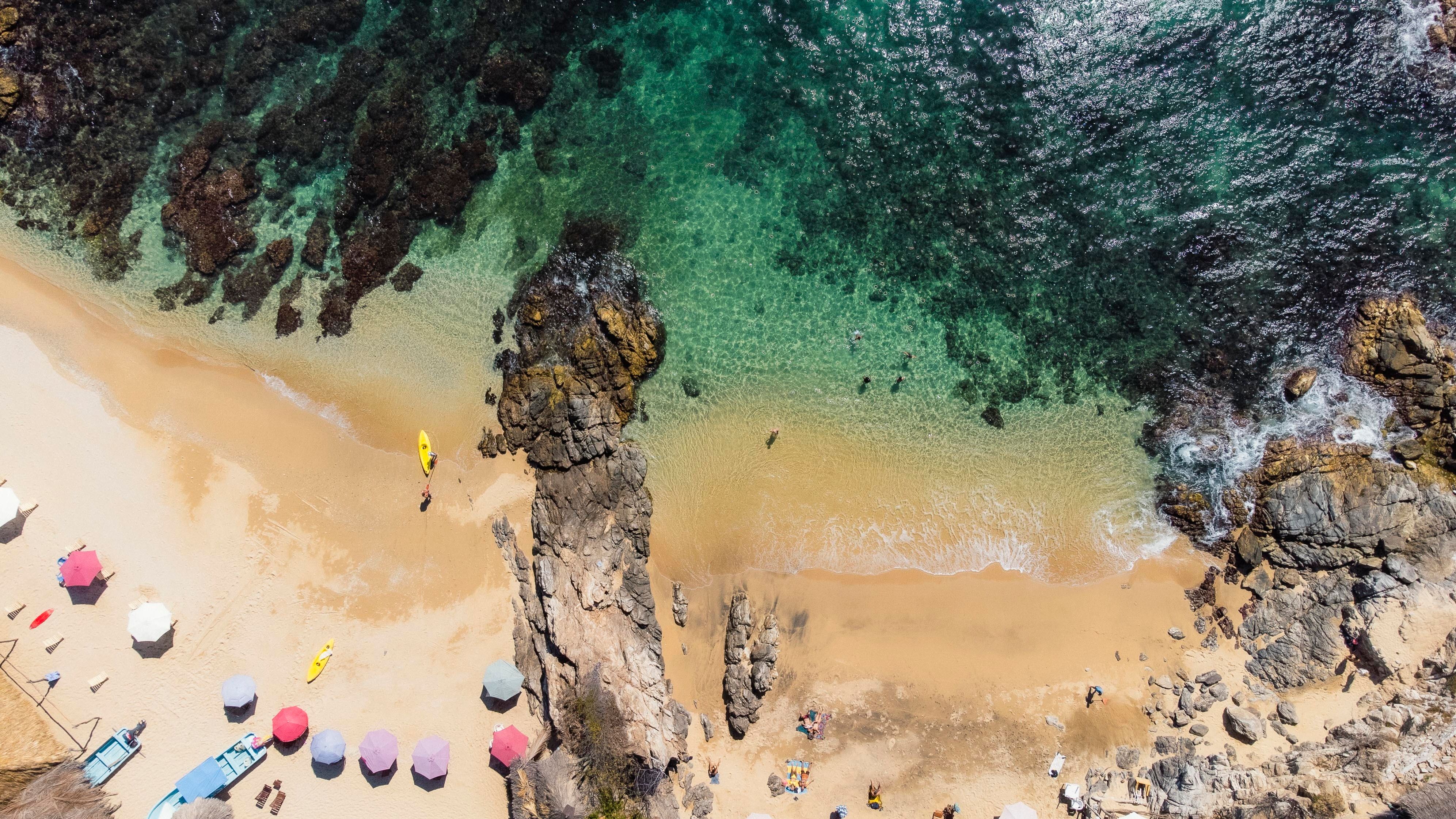 Aerial drone view of a rocky beach near Huatulco with turquoise water, showing the terrain typical of the bay road access