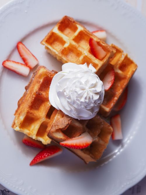 Free Golden waffles topped with fresh strawberries and a swirl of whipped cream on a white plate. Stock Photo