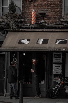 Two men converse outside a barbershop on a city street, a classic urban scene.