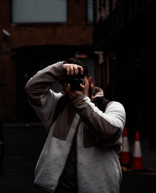 Man in Gray Coat Taking Picture with Black Camera
