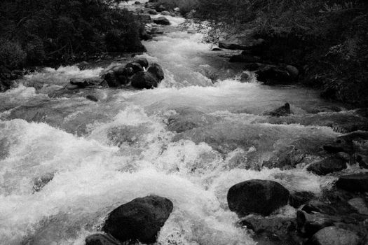Dynamic black and white image of river rapids cascading over rocks, capturing natural motion.
