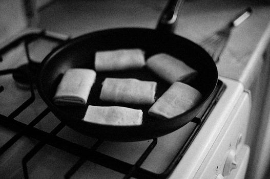Monochrome shot of food frying on a stovetop in a frying pan.