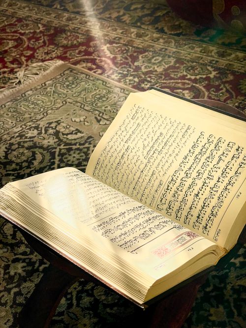 Free Open Quran with Arabic text illuminated by sunlight on an ornate carpet, symbolizing spirituality. Stock Photo
