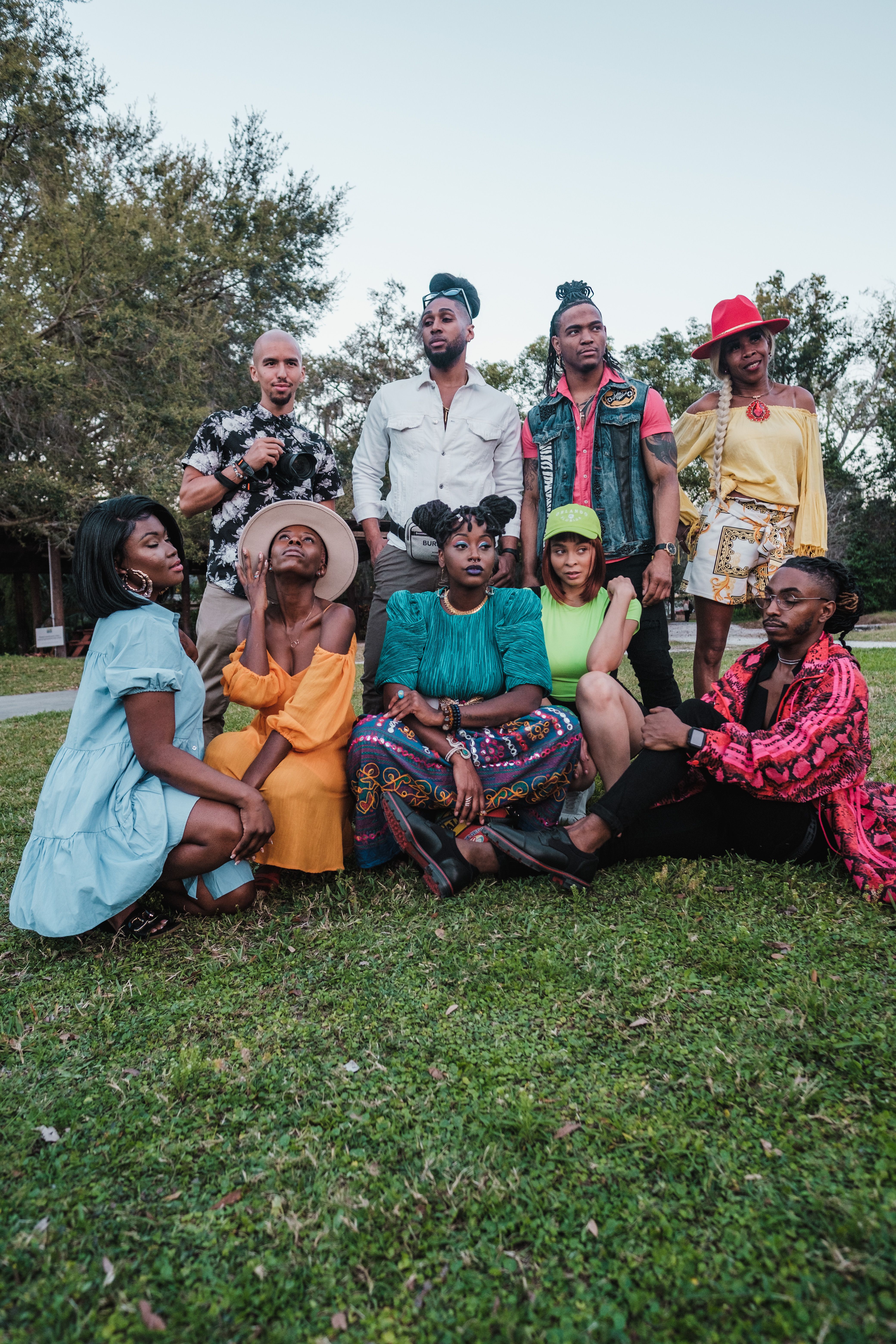A diverse group of adults posing outdoors in a park setting, showcasing colorful fashion and friendship.