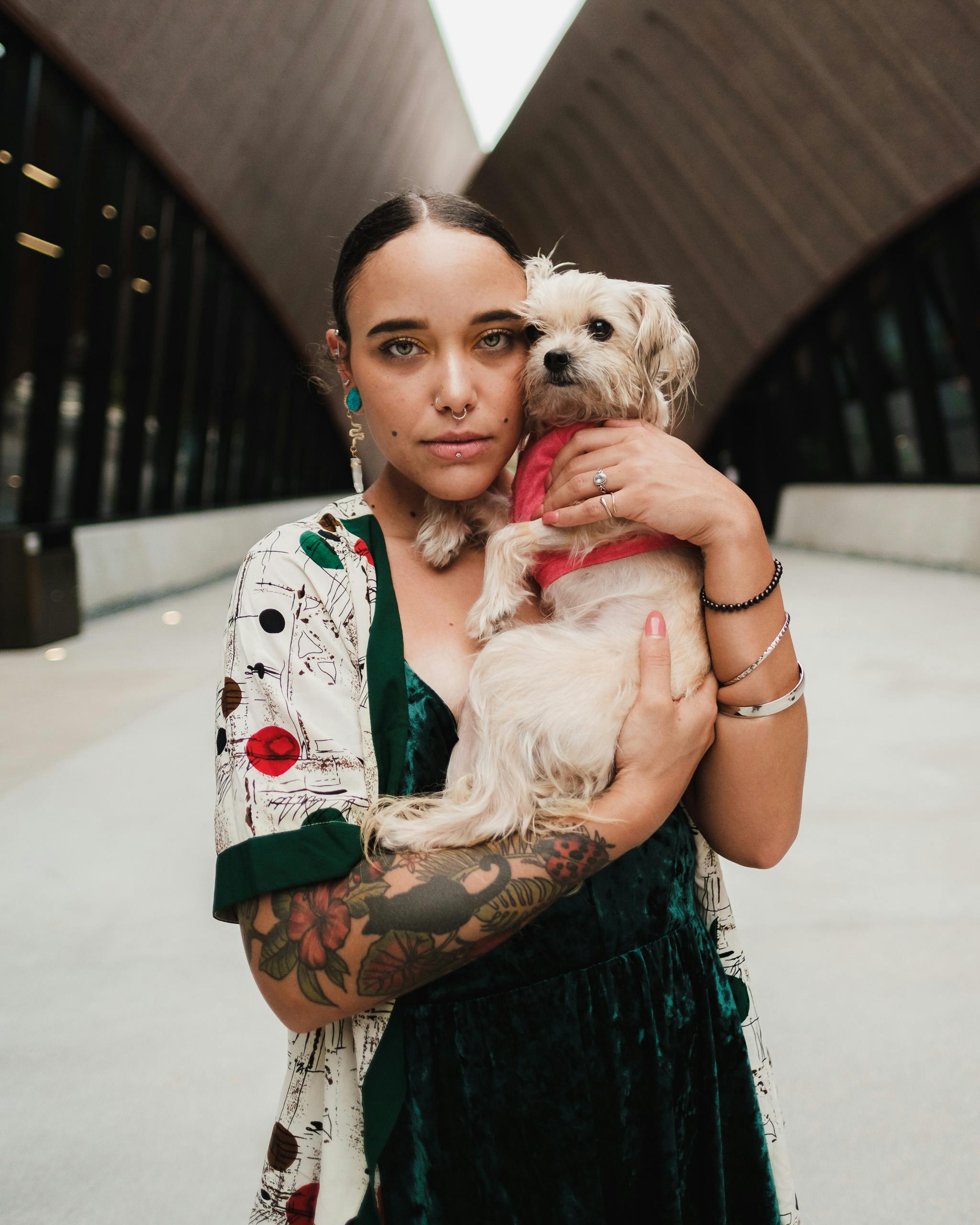 a tattooed woman hugging a white puppy while looking at the camera