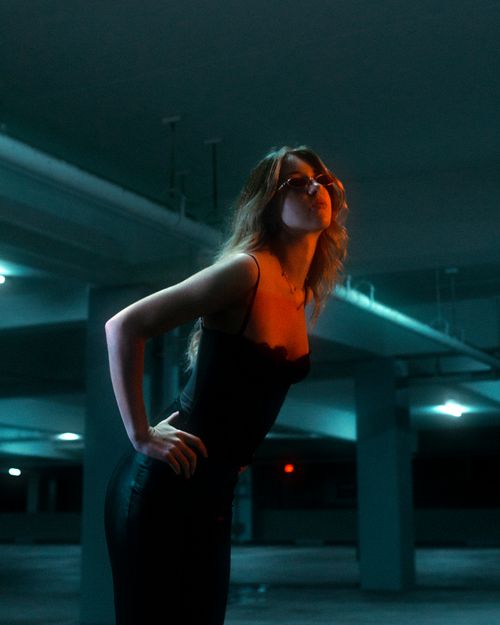 Free Fashionable woman posing confidently in dimly lit urban parking garage, showcasing modern elegance. Stock Photo