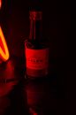 A moody shot of a Calem Port wine bottle illuminated by a red neon light against a dark background.
