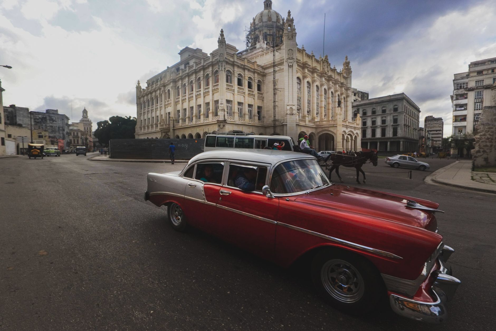 Vintage red car driving past historic architecture in Havana city scene.
