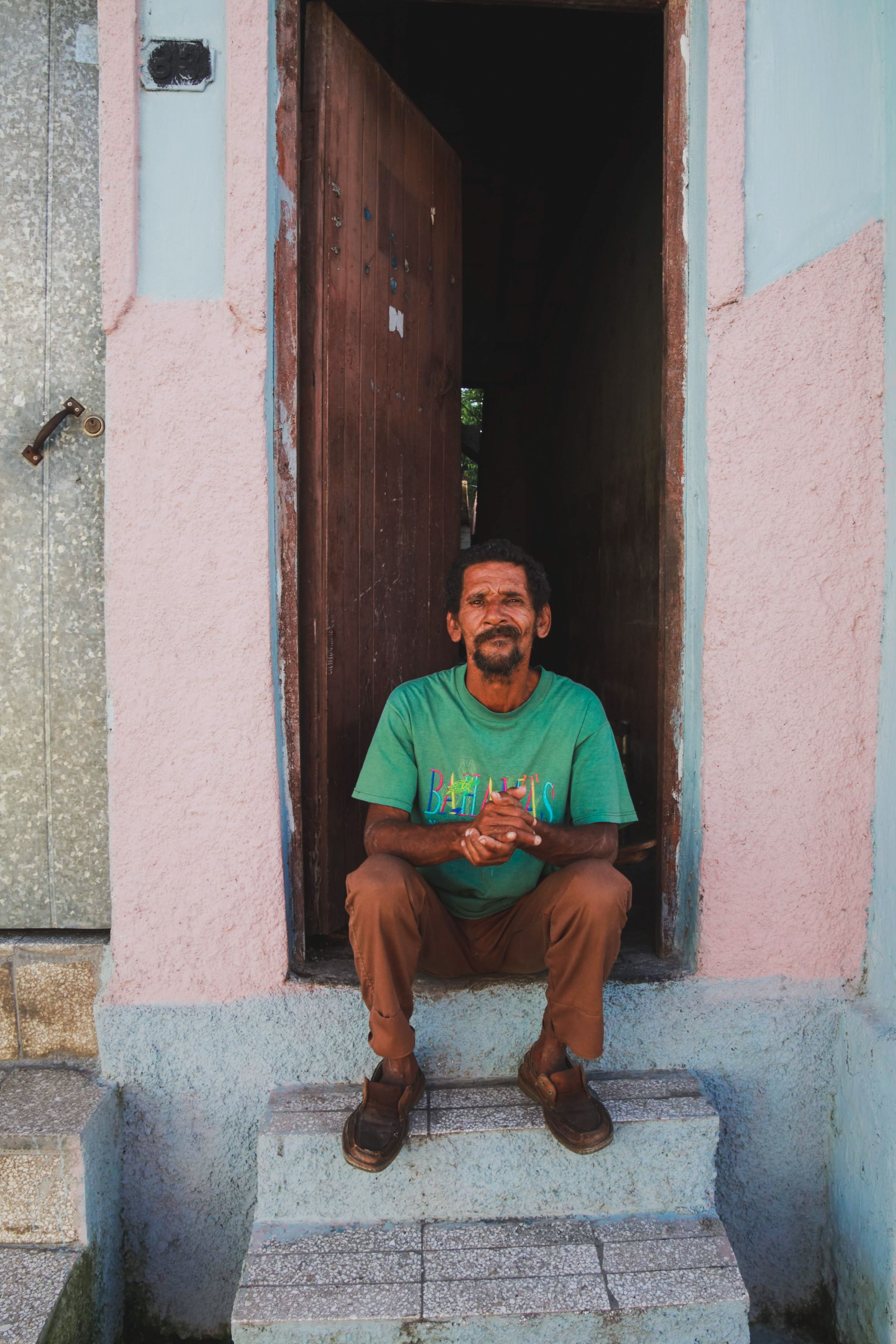 A man in casual attire sits comfortably in a doorway on stone steps during daytime.