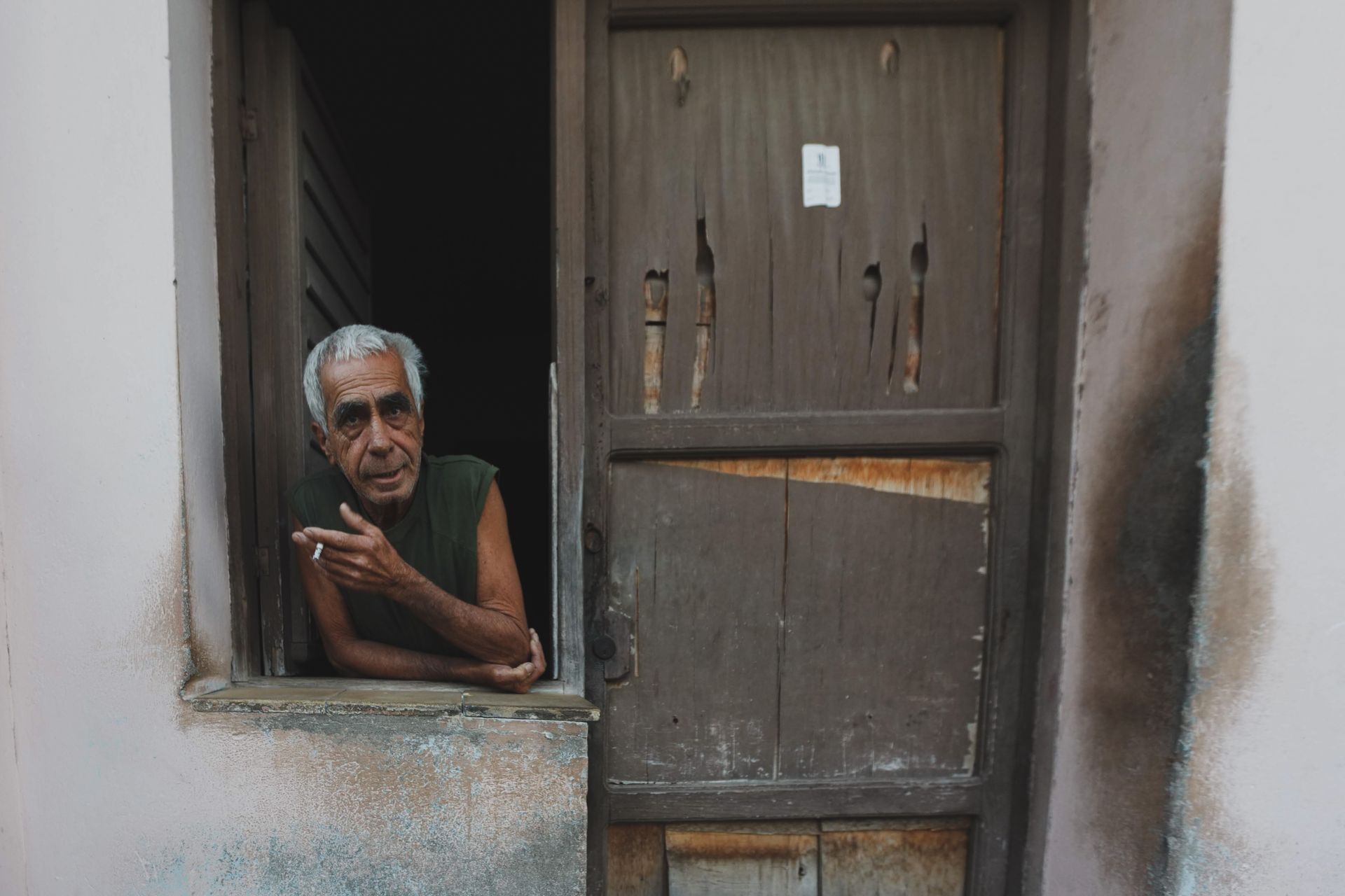 Elderly man with gray hair smoking in a rundown doorway, showcasing isolation and solitude.
