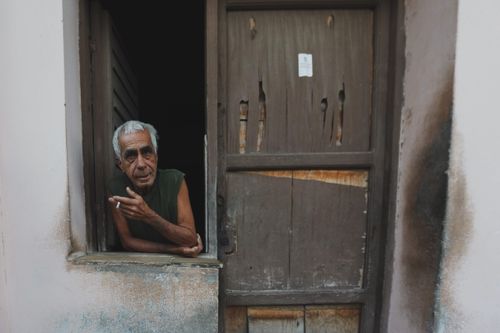 Free Elderly man with gray hair smoking in a rundown doorway, showcasing isolation and solitude. Stock Photo