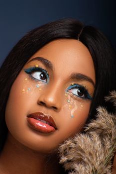 Close-up portrait of a woman with creative makeup and dried flowers, exuding elegance and glamour.