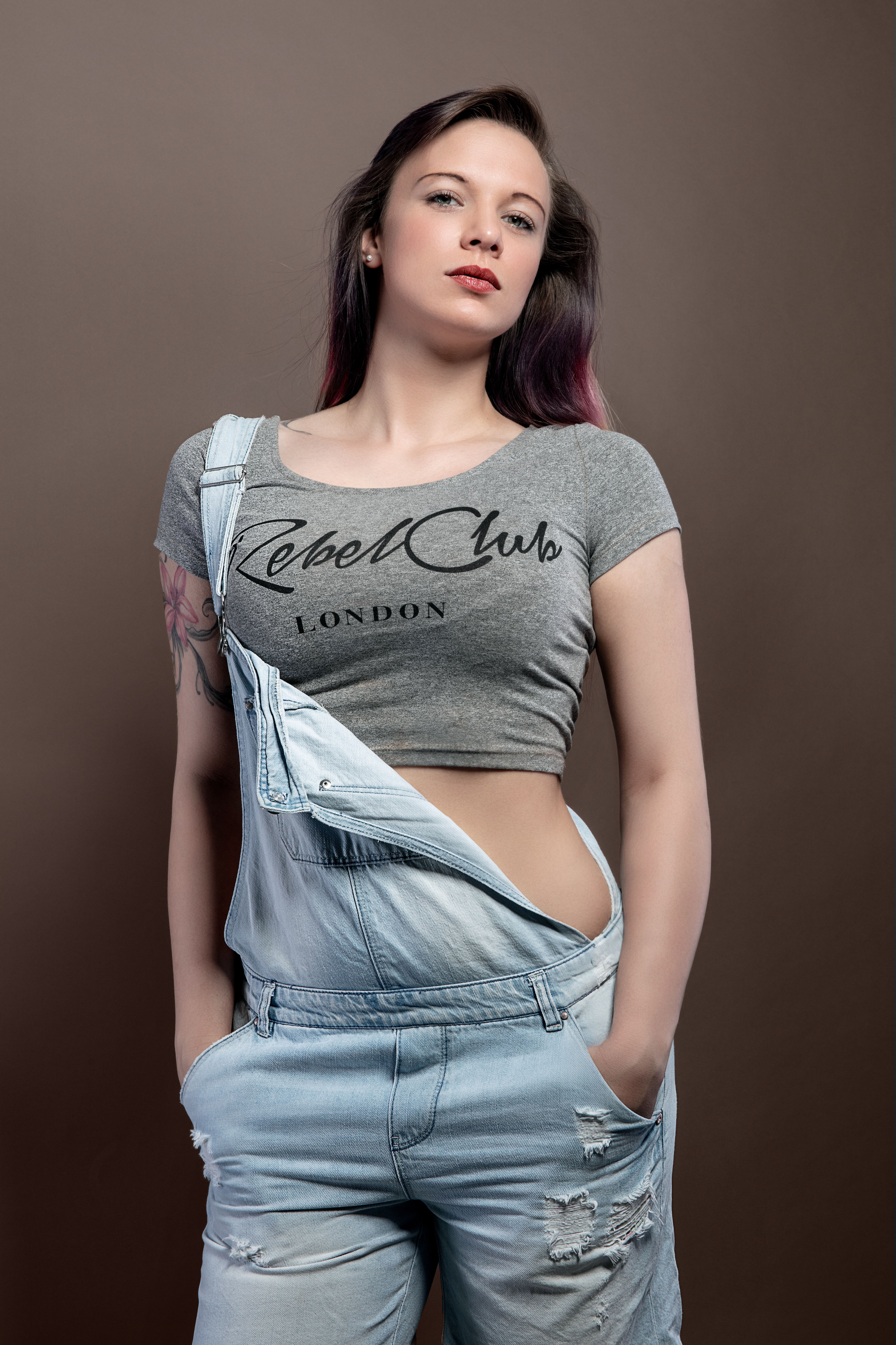 Stylish studio portrait of a woman in denim overalls and crop top posing confidently.