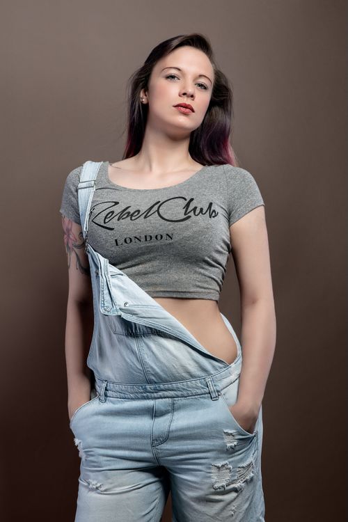 Free Stylish studio portrait of a woman in denim overalls and crop top posing confidently. Stock Photo