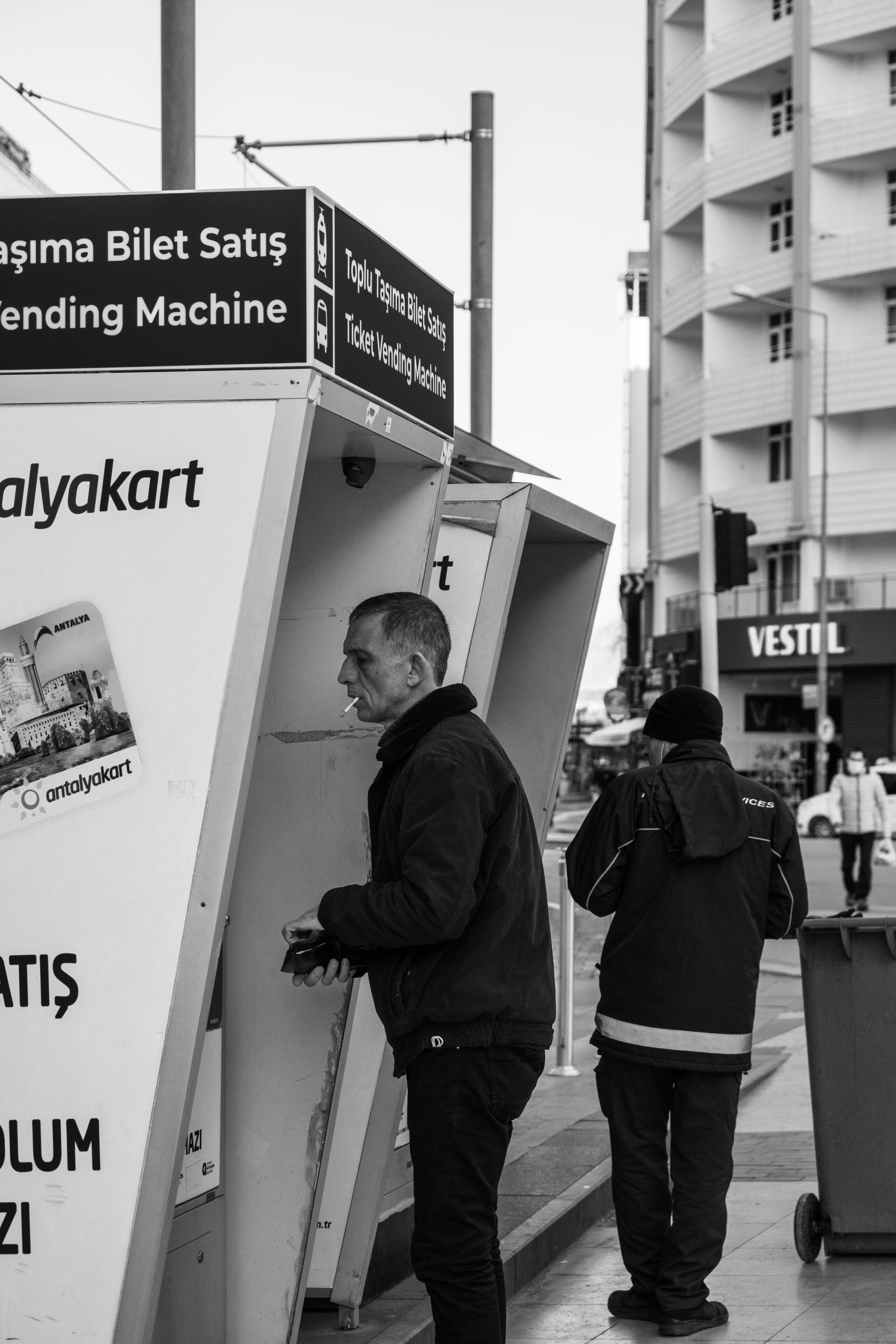 grayscale photo of a man standing near a ticket vending machine