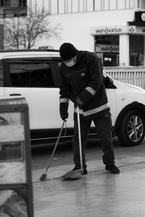 Monochrome Photo of a Man Sweeping Near a Car