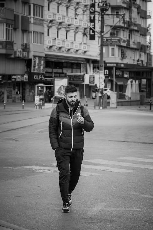 Grayscale Photo of a Man in a Puffer Jacket Walking