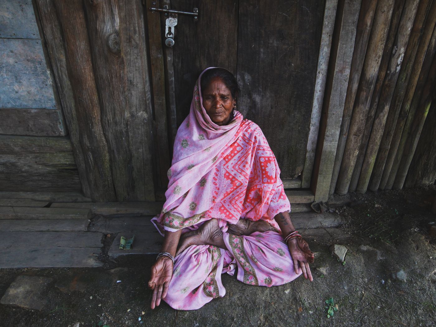 A senior Indian woman in traditional clothing meditating outdoors in a rural setting, reflecting mindfulness and emotional well-being.