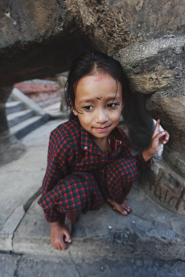 Little Girl In Pyjamas Crouching In Rock Cavity