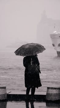 A woman stands with an umbrella by the sea in rainy Istanbul, capturing a moody atmosphere.