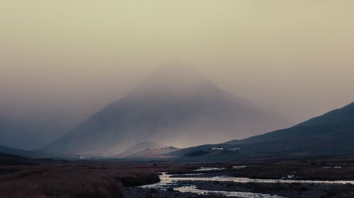 Free Serene landscape of misty mountain with a tranquil stream flowing beneath an overcast sky. Stock Photo