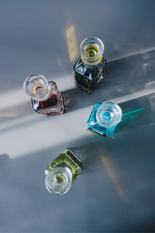Free Four colorful glass perfume bottles casting shadows on a table under sunlight. Stock Photo