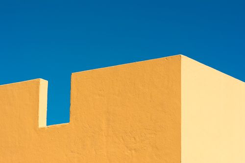 Free Modern minimalist architecture with a bold yellow facade against a clear blue sky. Stock Photo