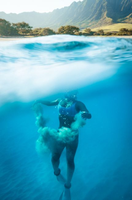 A woman snorkeling underwater in the clear turquoise waters of Hawaii, creating a stunning over-under photography effect.