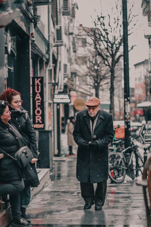 Free A bustling city sidewalk during snowfall, people in warm clothes walking by shops. Stock Photo