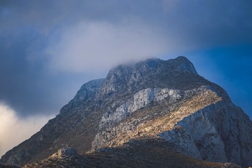 Free A towering rocky mountain peak partially shrouded in clouds under a dramatic blue sky, captured outdoors. Stock Photo