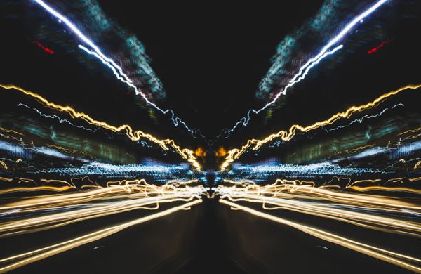 Long-exposure light trails converging down a night road. Photo by Nothing Ahead on Pexels.