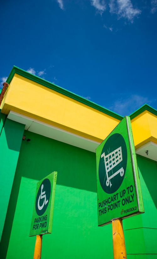 Free Green and yellow building facade with PWD and shopping cart signs against a blue sky. Stock Photo