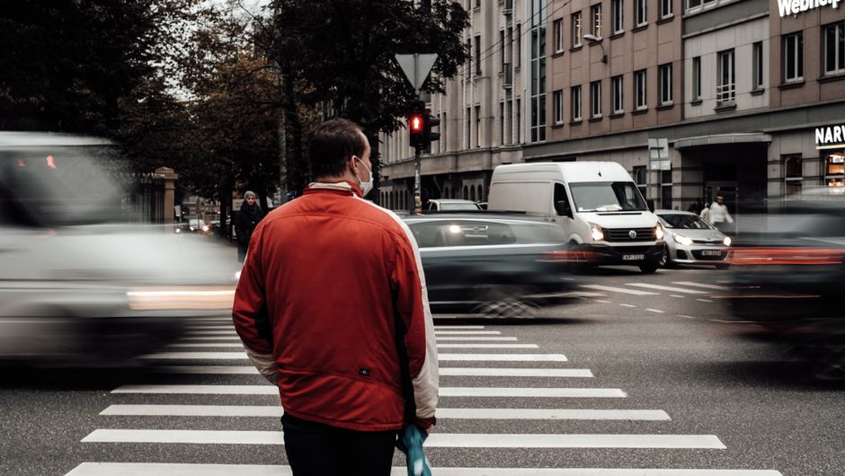 Man in red jacket at a busy pedestrian crossing in Riga, Latvia during the day.