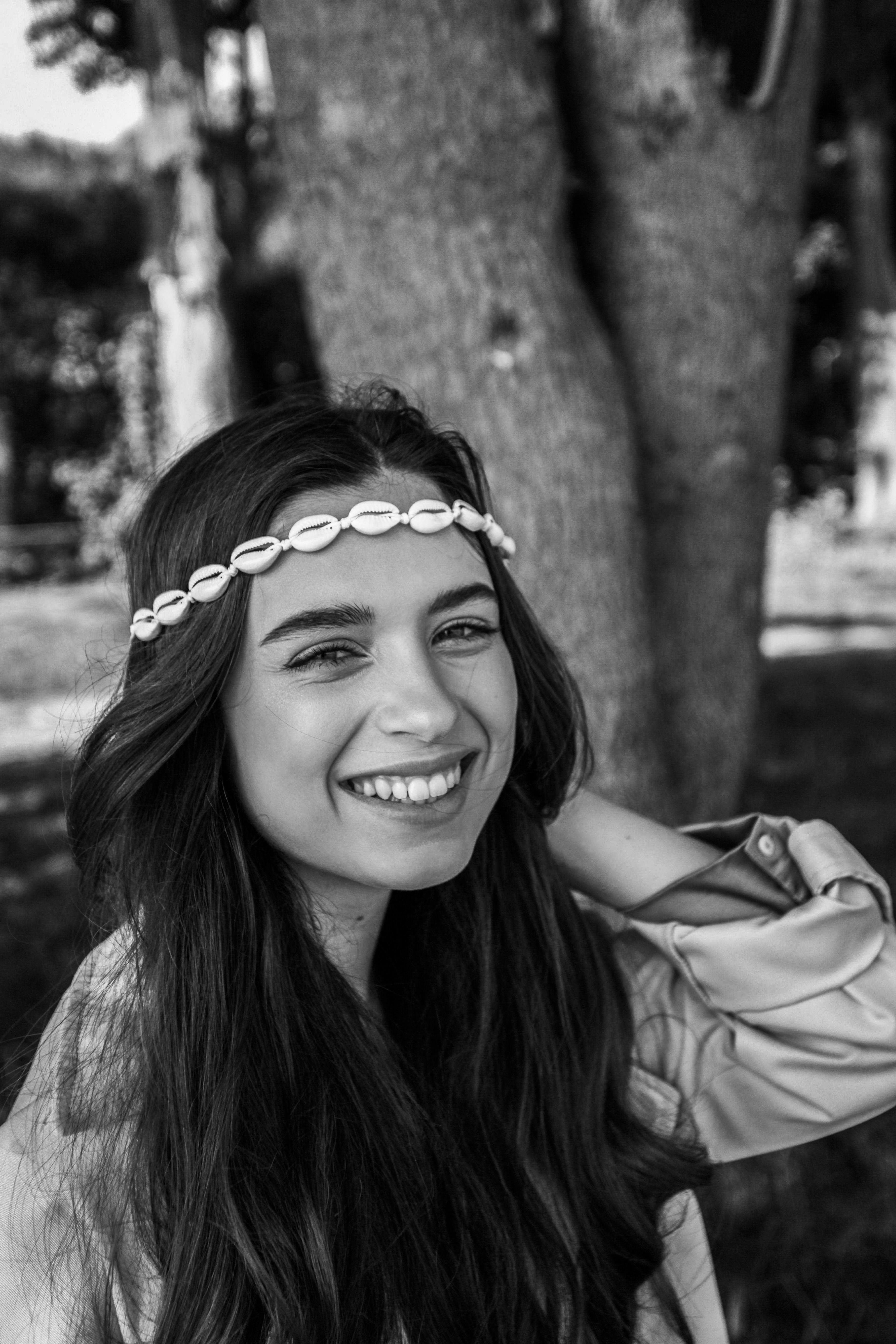 Black and white portrait of a smiling woman wearing a seashell hairband outdoors.