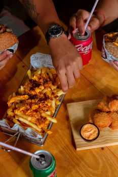 Hands enjoying burgers, fries, and soft drinks at a casual meal gathering.