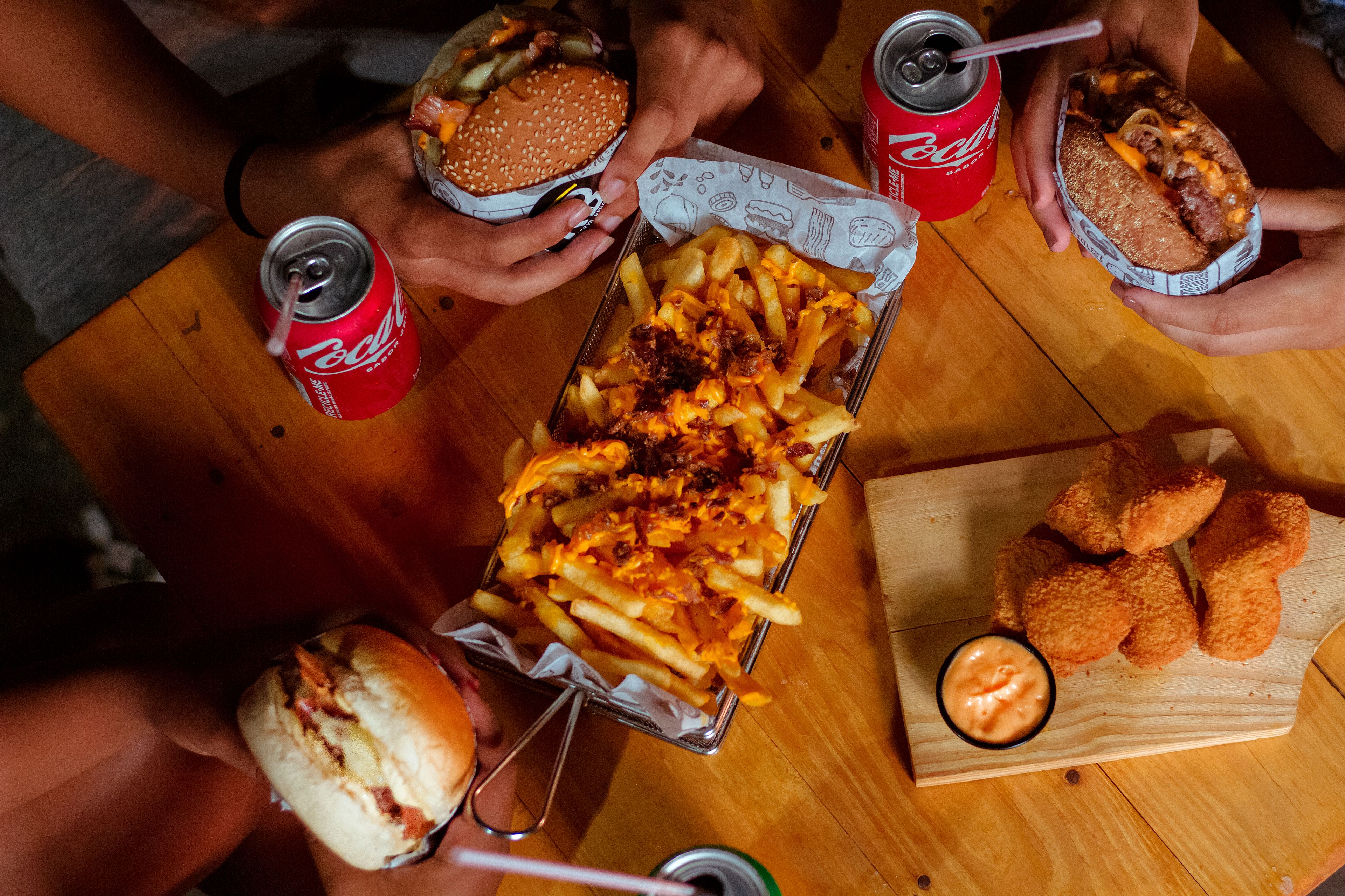 Delicious fast food spread featuring burgers, fries, nuggets, and drinks on a wooden table.
