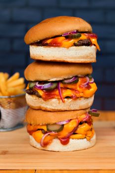 Close-up of stacked cheeseburgers with cheese, pickles, onions, and fries on a wooden surface.