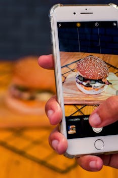 Close-up of a burger being photographed with a smartphone indoors.