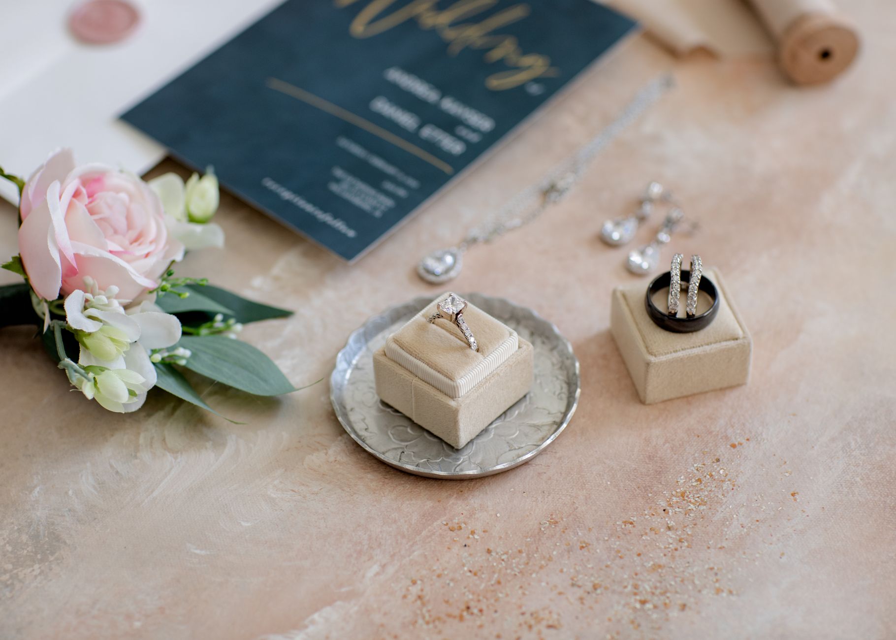 Top-down view of wedding jewelry alongside floral arrangement and invitation.