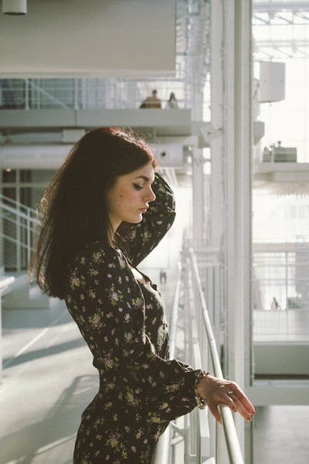 Profile view of a woman in a floral dress by a railing indoors with natural light.