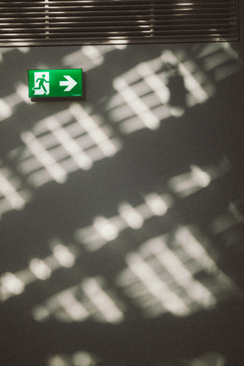 Free Green emergency exit sign on a wall with abstract shadow patterns, creating a unique visual texture. Stock Photo