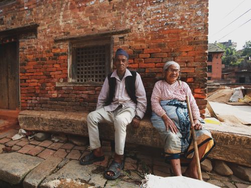 Free Senior couple sitting against an old brick wall in a rustic outdoor setting. Stock Photo