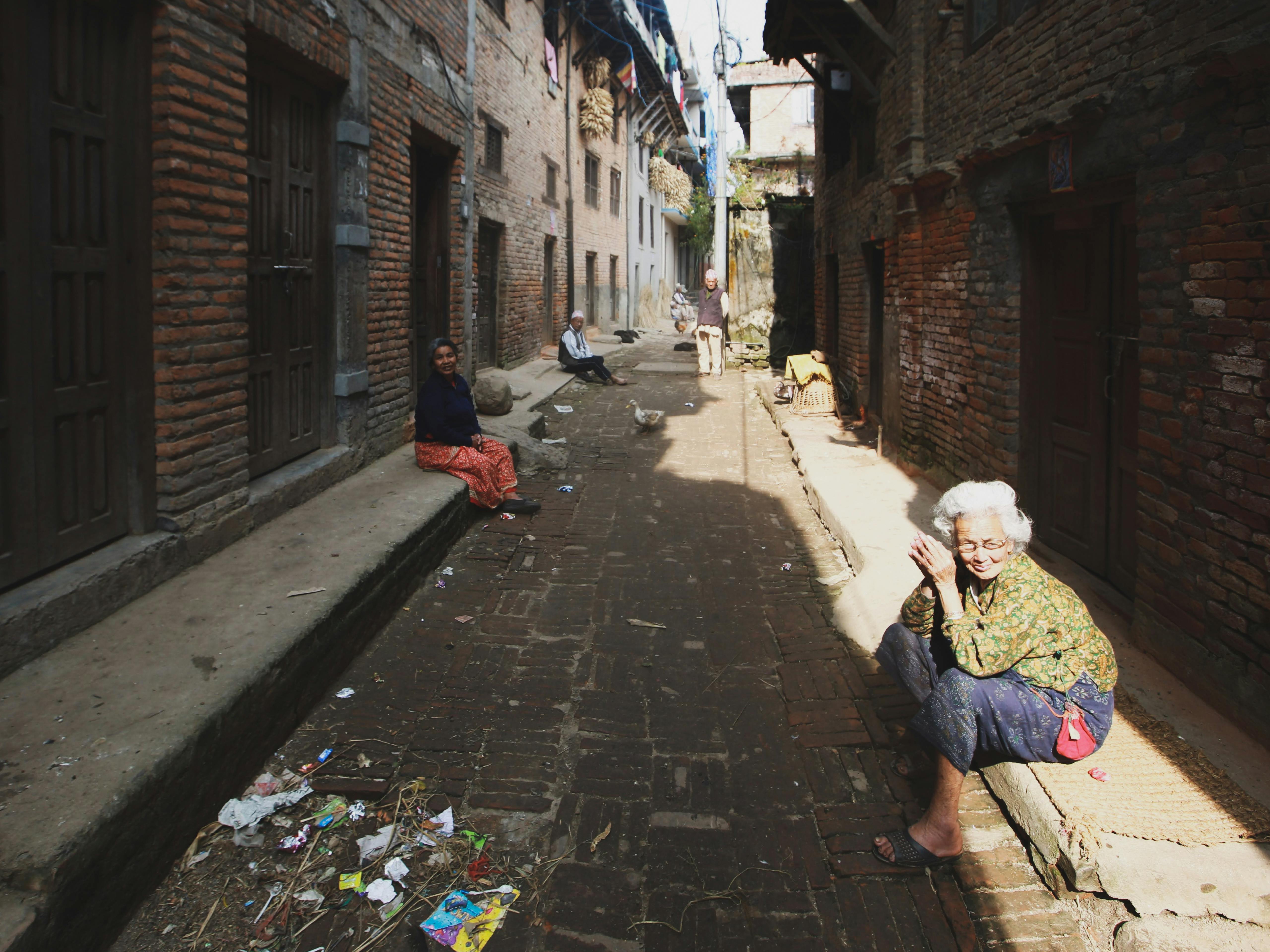 A narrow alleyway in a historical town with senior residents sitting and enjoying the sunny day.