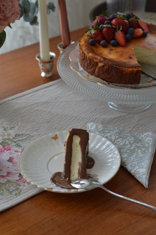 Free A delightful slice of cheesecake with chocolate on a plate, with a berry-topped cheesecake on display. Stock Photo