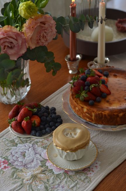 A beautifully decorated dessert table featuring a cheesecake, fresh berries, flowers, and candles, perfect for celebrations.