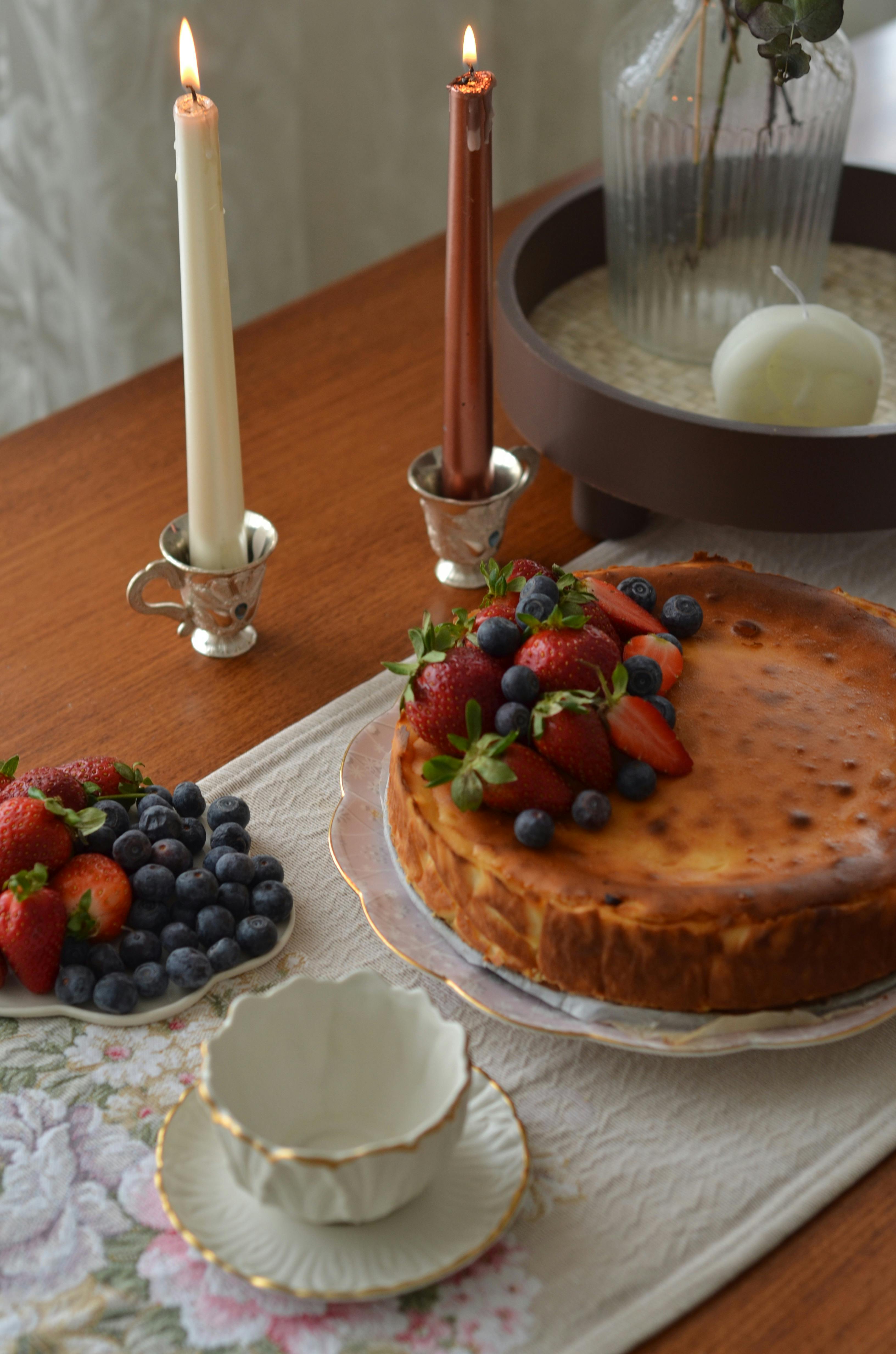 A luscious cheesecake garnished with berries, presented on a table adorned with candles for a cozy dining experience.