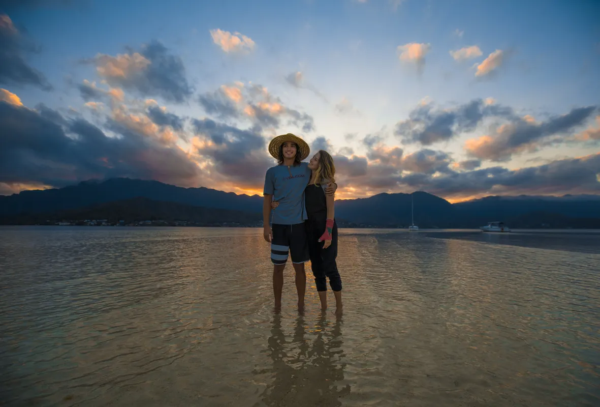Couple walking barefoot along a Hawaiian beach at sunset on their honeymoon