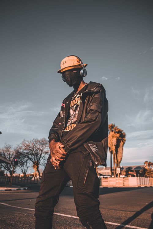 Free A man in trendy streetwear and headphones stands moody on a Namibian street, blending fashion with urban vibes. Stock Photo